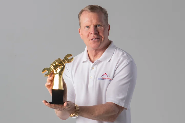 Paul Donahue, wearing Advanced Digital Automotive Group's white polo shirt, scamming the Golden Wrench Award trophy.